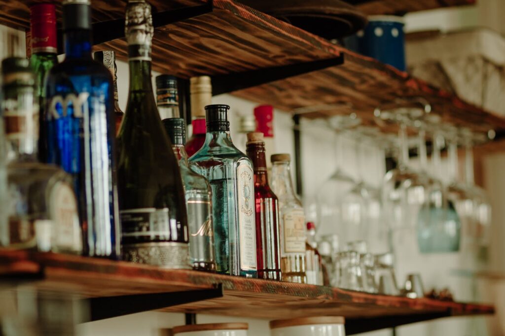 A collection of alcoholic beverage bottles on a rustic wooden bar shelf
